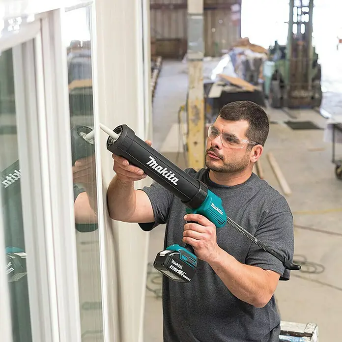 Makita LXT 18V Akku-Kartuschenpresse DCG180ZX - 18 V, Li-Ionen, Ohne Akku - Ein Handwerker verwendet eine Makita Akku-Kartuschenpistole, um Dichtungsmasse auf ein Fenster aufzutragen.