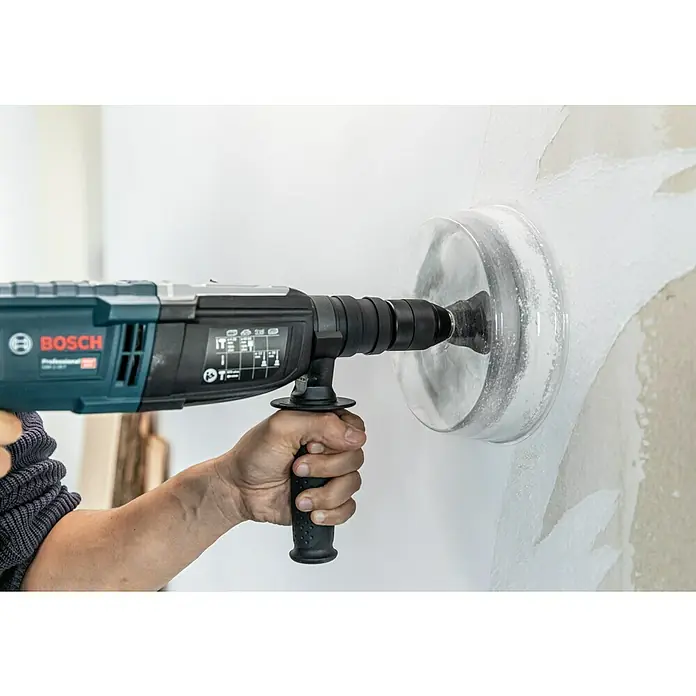 Craftomat Lochsäge Verstellbar - Verstellbar - Ein Bosch Bohrhammer mit Staubabsaugung bohrt ein Loch in eine weisse Wand. Das Werkzeug ist mit einem Griff für zusätzliche Kontrolle ausgestattet.