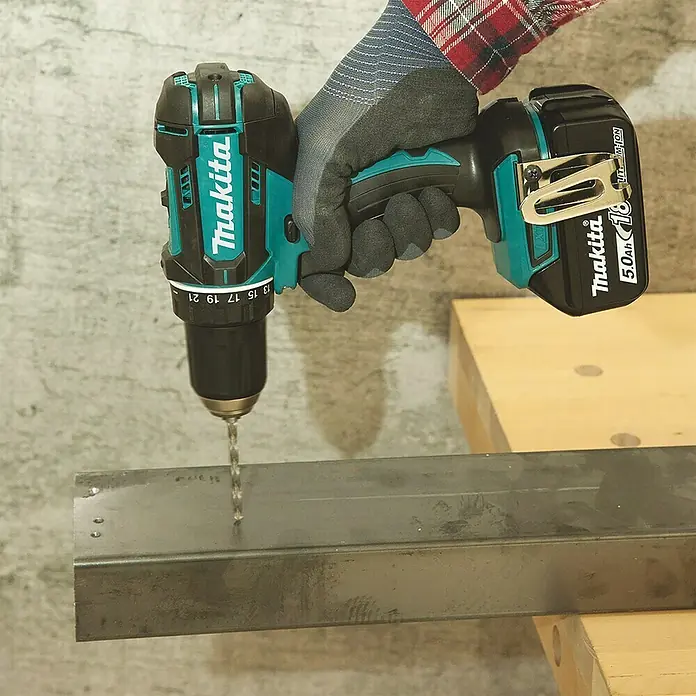 Makita LXT 18V Akku-Bohrschrauber DDF482RFJ - 18 V, 2 Akkus, 3 Ah, 62 Nm - Eine Makita Akku-Bohrmaschine im Einsatz, die ein Loch in ein Metallstück bohrt. Die Bohrmaschine ist schwarz und türkis und verfügt über einen 5.0Ah Akku.