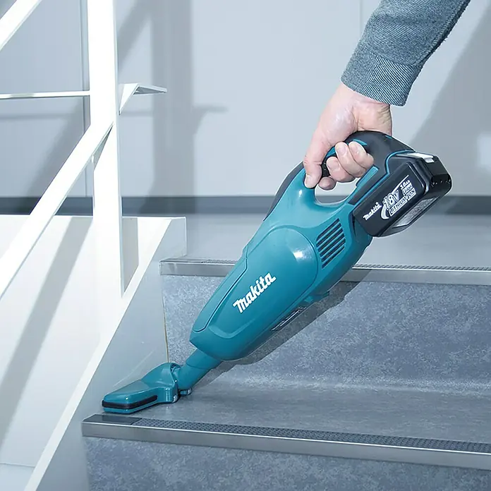 Makita LXT 18V Akku-Staubsauger DCL182Z - 18 V, Ohne Akku - Ein türkisfarbener Makita Akku-Staubsauger wird auf einer Treppe verwendet, der eine einfache und kabellose Reinigung ermöglicht.