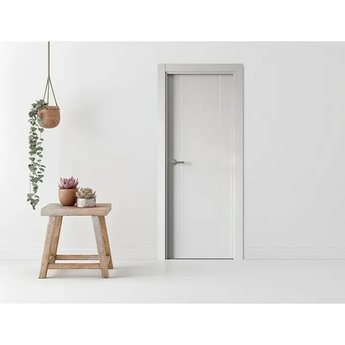 Pack puerta de interior Natal - 82,5 x 203 cm, Derecha, Blanco - Elegante puerta interior blanca con paneles verticales y manija moderna en una habitación luminosa, junto a un taburete de madera con plantas.