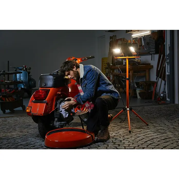 Ledvance LED-Arbeitsleuchte - 5.400 lm, Lichtfarbe: Kaltweiß, Anzahl Leuchtmittel: 2 Stk. - Ein Mann wartet einen orangefarbenen Motorroller in einer Garage mit einer orangefarbenen Arbeitsleuchte mit zwei LED-Lampen.