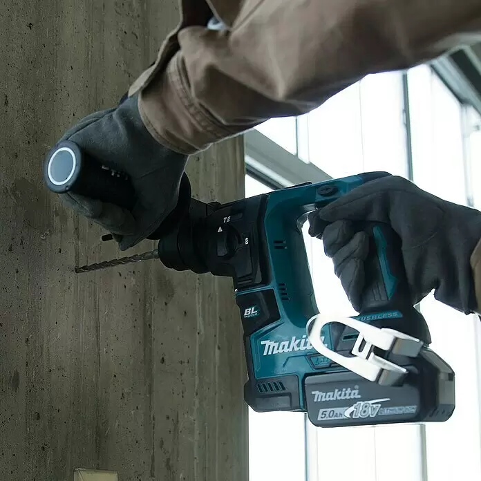 Makita LXT 18V Akku-Bohrhammer DHR171RAJ - 18 V, 2 Akkus, 1,2 J - Ein Arbeiter bohrt mit einem tealfarbenen und schwarzen Makita Akku-Bohrhammer mit 5.0Ah 18V Akku in eine Betonwand.