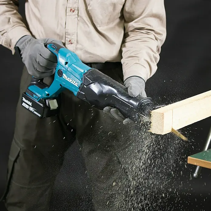 Makita LXT 18V Akku-Säbelsäge DJR186ZK18 V, Ohne Akku, Leerlaufhubzahl: 0 /min - 2.800 /min - Nahaufnahme einer Makita Akku-Säbelsäge beim Schneiden von Holz, mit Fokus auf Präzision und Staubentwicklung.