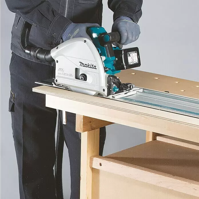 Makita LXT 18V Akku-Tauchsäge DSP601ZJU - 18 V, Ohne Akku, 2.500 U/min - 6.300 U/min - Person schneidet mit einer weißen und türkisen Makita Tauchsäge und Führungsschiene eine Holzplatte auf einer Werkbank, mit Staubabsaugung.