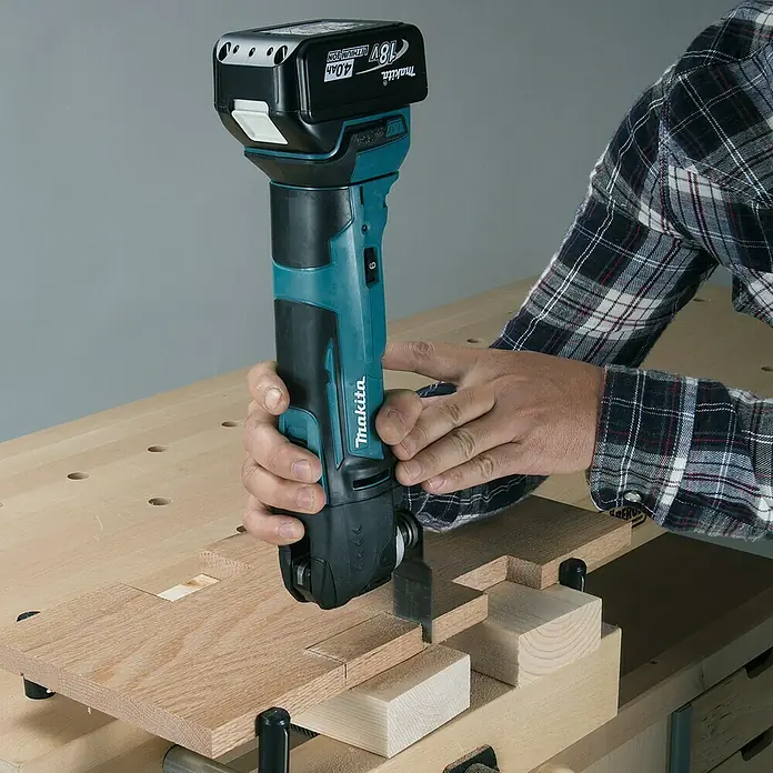 Makita LXT 18V Akku-Rotationswerkzeug DTM51Z - 18 V, Li-Ionen, Ohne Akku - Der Makita Akku-Multifunktionsschneider wird auf einer Werkbank zum Schneiden von Holz verwendet. Das Gerät ist mit einem 18V Akku ausgestattet.