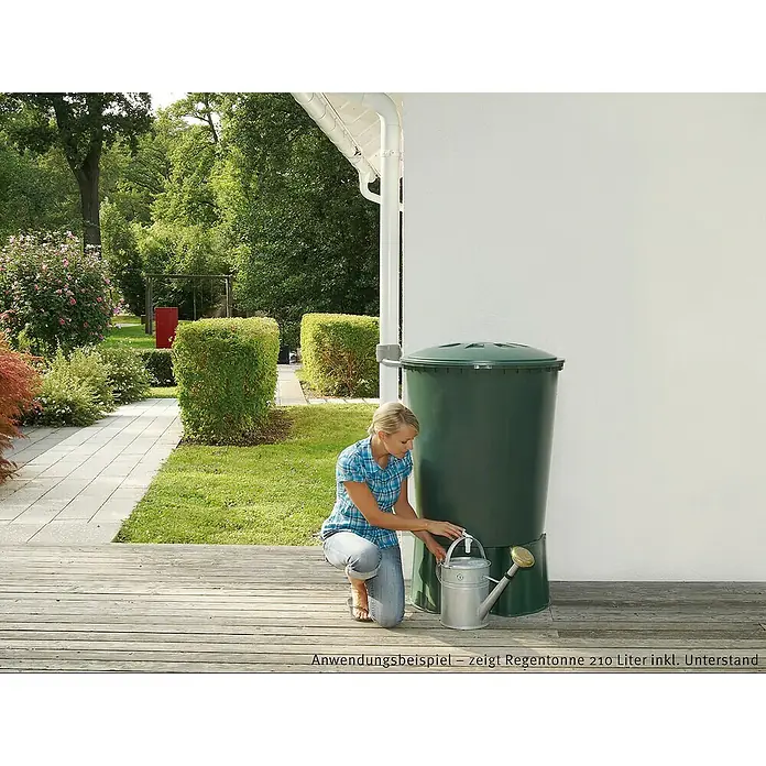 Garantia Basic Line RegentonnensockelPassend für: 510 l Regentonnen Rund, Grün - Eine Frau befüllt eine Gießkanne an einer Regentonne im Garten, die das aufgefangene Regenwasser speichert.
