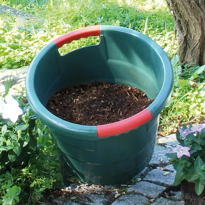 Garantia Tragebehälter - 45 l - Ein grüner Pflanzkübel mit roten Griffen, gefüllt mit Erde, steht im Garten, umgeben von Pflanzen. Ideal für Gartenarbeit!