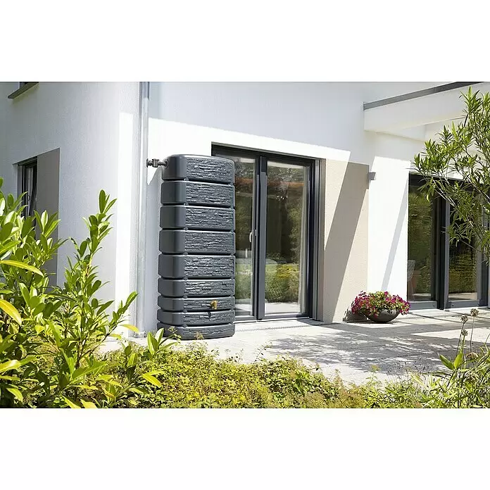 4rain Regenspeicher Slim Stone - 500 l, Grau - Dunkelgraues Regenwassertank im Schichtstein-Design, an ein Fallrohr angeschlossen, auf einer Terrasse zur Regenwassernutzung.