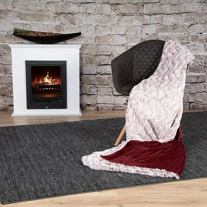 Decke Smooth - Rot, 200 x 150 cm, 100 % Polyester - Nahaufnahme eines Zimmers mit einem eleganten Sessel, auf dem eine weiche Decke liegt, und einem modernen Kamin.