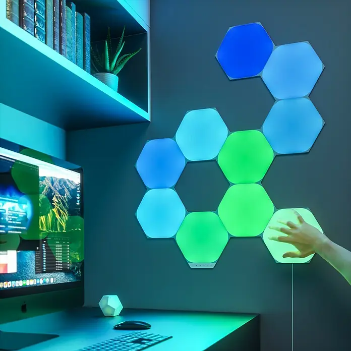 Nanoleaf Erweiterungskit Shapes Hexagons 3 Panels3 Stk., Weiß, RGBW, Hexagons, Smart Home-fähig: Ja - Bunte hexagonale LED-Panels an einer Wand, die ein spielerisches und modernes Ambiente schaffen. Eine Hand berührt ein Panel.