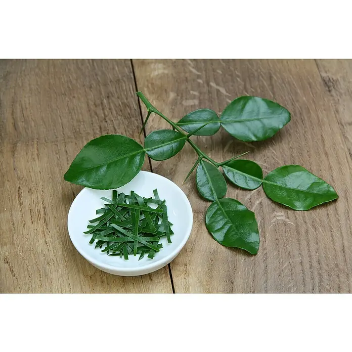 Blu Bio Kaffir-Limettenbaum - Citrus hystrix, Weiß, Topfgröße: 12 cm - Ein Teller mit geschnittenen Kaffernlimettenblättern und einem Zweig auf einem Holztisch. Die Blätter sind frisch und grün.
