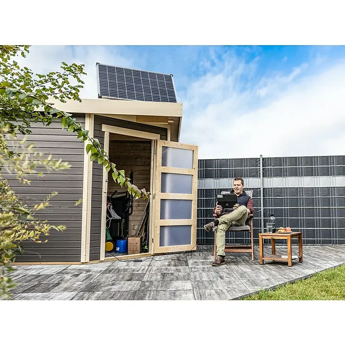 Offgridtec Solarmodul 0% MwSt. (gem. § 12 Abs. 3 UStG) - Nennleistung: 150 W, 114 x 68 x 3,5 cm, 1 Stk. - Moderne Gartenlaube mit Solarpanel auf dem Dach, neben der ein Mann mit Laptop sitzt, ideal für den umweltbewussten Gartenbesitzer.