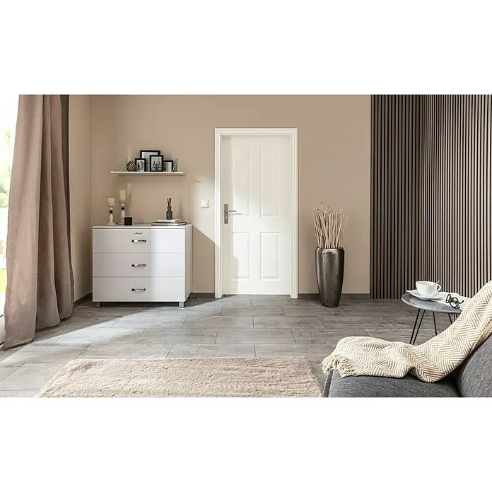 Kilsgaard Zimmertür 20/04 - 860 x 1.985 mm, DIN Anschlag: Links, Weiß lackiert, ähnlich RAL 9010, Vollspan - Dieses moderne Interieur zeigt eine weiße Kommode mit drei Schubladen neben einer Tür, ergänzt durch stilvolle Dekoration und Wandpaneele.