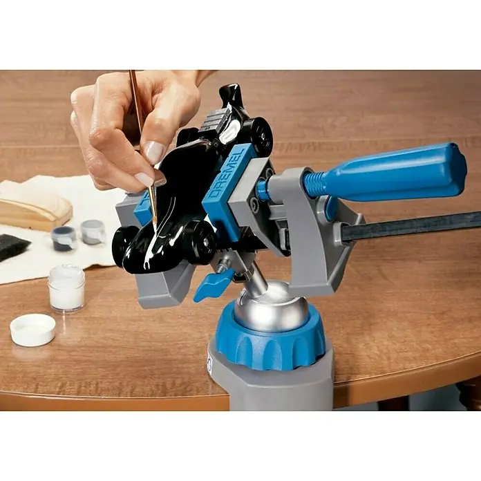 Dremel Multi-Schraubstock 2500 - Neigungswinkel 50 ° - Detailaufnahme eines Dremel-Werkzeughalters in Gebrauch, der ein kleines, schwarzes Objekt beim Bemalen fixiert.
