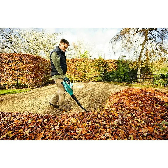 Bosch Power for All 18V Akku-Heckenscheren-Set EasyHedgeCut 18-45 + ALB 18 LI - 18 V, 2 Ah, Li-Ionen - Ein Mann benutzt einen Laubbläser im Garten, um die Blätter zu entfernen. Der Fokus liegt auf dem Laubbläser.