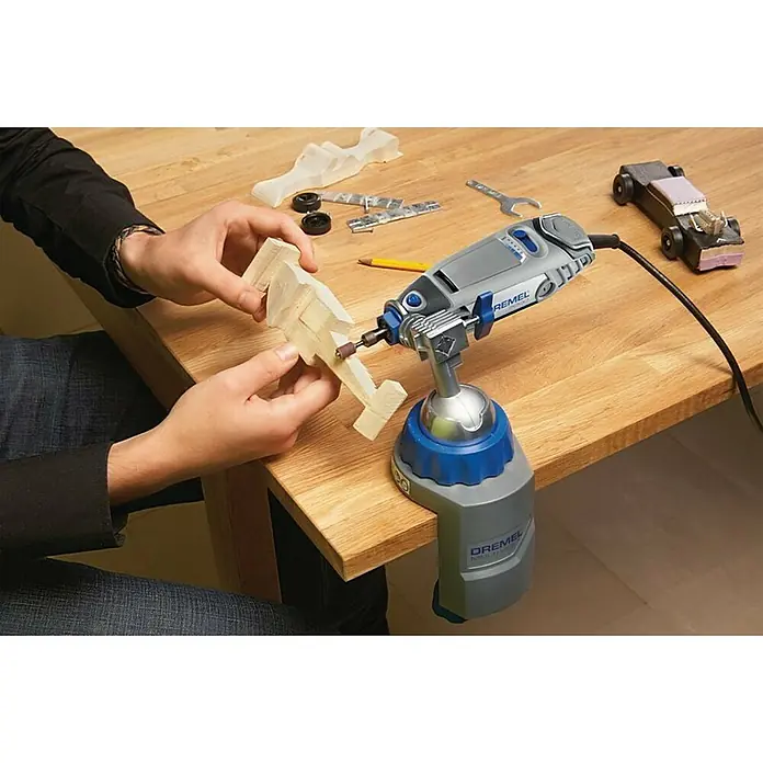 Dremel Multi-Schraubstock 2500 - Neigungswinkel 50 ° - Nahaufnahme eines Dremel-Werkzeugs, das an einer Tischkante befestigt ist, während eine Person ein Holzstück bearbeitet.