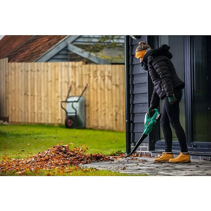 Bosch Power for All 18V Akku-Heckenscheren-Set EasyHedgeCut 18-45 + ALB 18 LI - 18 V, 2 Ah, Li-Ionen - Eine Frau benutzt einen Laubbläser, um Blätter zu entfernen. Das Gerät ist grün und hat einen Akku für kabellose Freiheit.