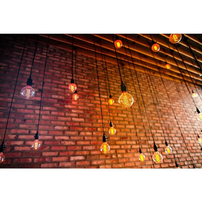 Müller-Licht Tint LED-Lampe Edison Retro - E27, Dimmbar, Warmweiß, 380 lm, 5,5 W - Dekorative Edison-Glühbirnen mit warmem Licht hängen vor einer rustikalen Ziegelwand und erzeugen eine gemütliche Atmosphäre.
