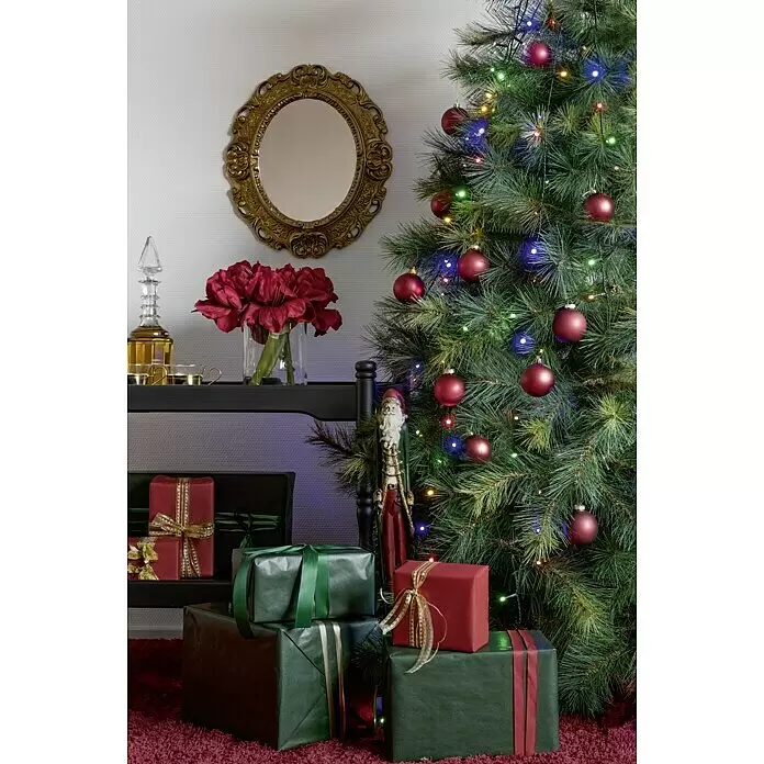 Konstsmide Baummantel - Innen, 2,4 m, 5 Stränge à 40 bunte LEDs - Eine festliche Weihnachtsszene mit geschmücktem Baum, rot-grünen Geschenken und einer Weihnachtsmannfigur auf rotem Teppich.