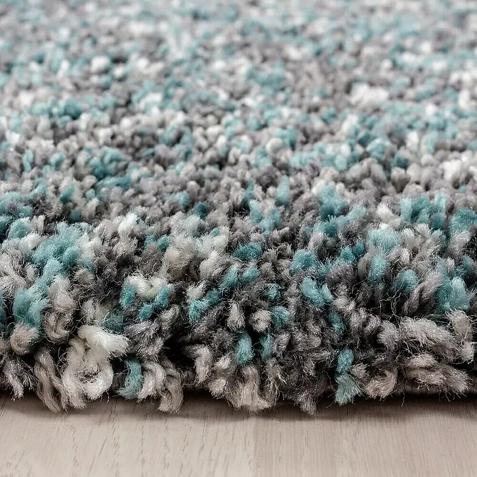 Hochflorteppich Enjoy 4500Blau, 290 x 200 cm, 100 % Polypropylen - Nahaufnahme eines flauschigen Teppichs mit grauen, türkisfarbenen und weißen Fasern, der eine weiche Textur und ein modernes Design zeigt.