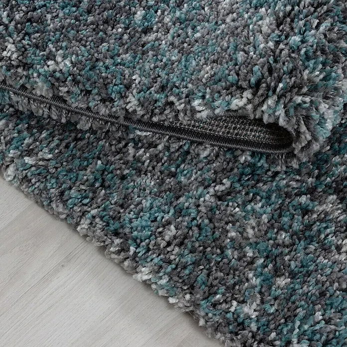 Hochflorteppich Enjoy 4500Blau, 290 x 200 cm, 100 % Polypropylen - Nahaufnahme eines grauen Teppichs mit türkisfarbenen Akzenten. Der Teppich hat eine hohe Florhöhe und ist auf einer hellen Oberfläche platziert.
