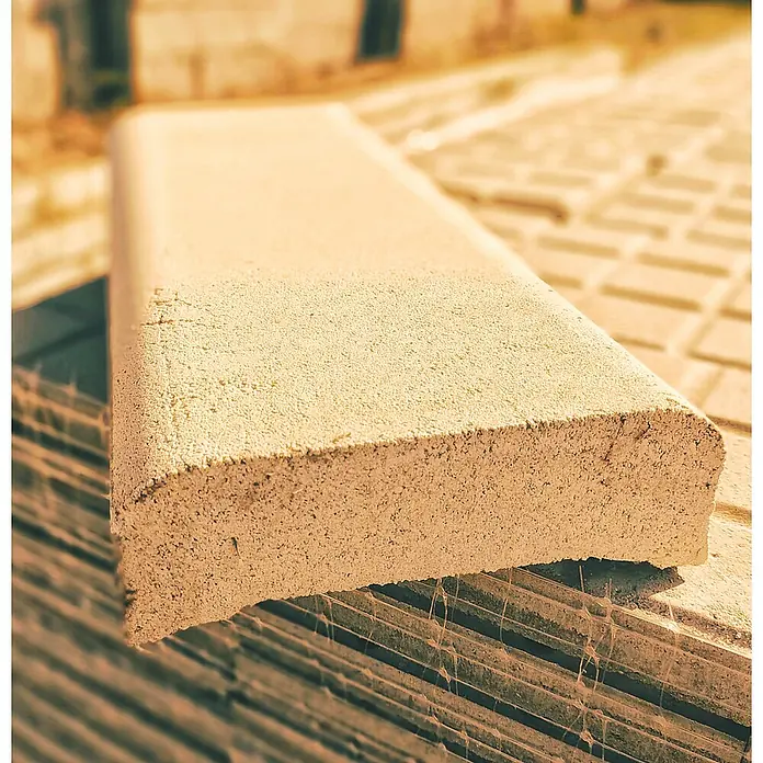 BHS Cataluña Cubremuros Jaen - 50 x 15 x 6 cm, Crema, Hormigón - Primer plano de un solo adoquín con un borde redondeado en una pila de otros adoquines al aire libre.