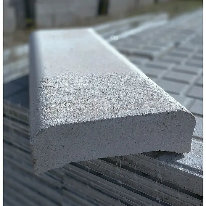 BHS Cataluña Cubremuros Jaen - 50 x 15 x 6 cm, Gris, Hormigón - Primer plano de un solo bordillo de hormigón gris con un borde redondeado, apilado con otros bordillos.