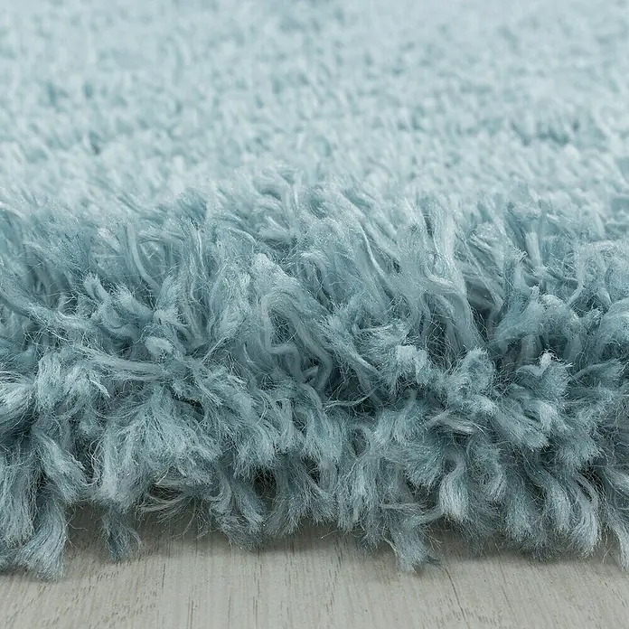 Hochflorteppich Fluffy 3500Blau, Durchmesser: 120 cm, 100% Polypropylen - Nahaufnahme eines hellblauen, zotteligen Teppichs, der eine weiche und einladende Textur zeigt.\n