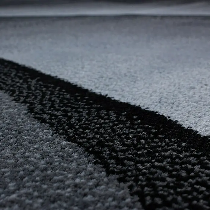 Kurzflorteppich Plus 8010 - Schwarz, 230 x 160 cm, 100% Polypropylen - Detailansicht eines modernen Teppichs mit einem markanten schwarzen Streifenmuster auf grauem Grund, das eine stilvolle Textur erzeugt.