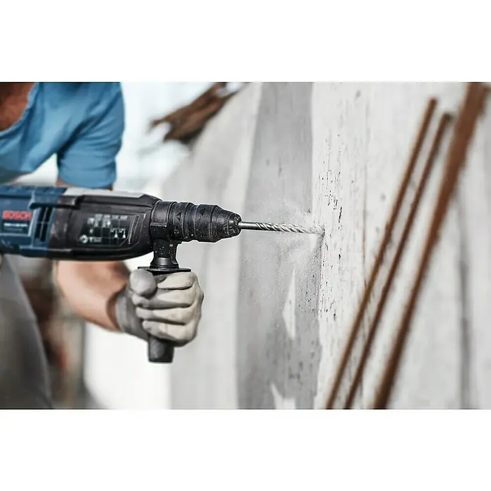 Bosch SDS-Plus-Bohrer- & Meißel-Set - 11 -tlg. - Ein Bauarbeiter benutzt einen Bosch Bohrhammer, um ein Loch in eine Betonwand zu bohren, wobei Staub und Partikel entstehen.