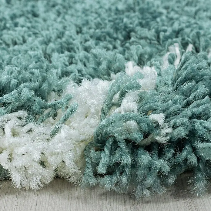 Hochflorteppich Alvor 3401Blau, Durchmesser: 200 cm, 100% Polypropylen - Nahaufnahme eines türkisfarbenen und weißen Shaggy-Teppichs, der eine weiche Textur und ein einladendes Gefühl vermittelt.