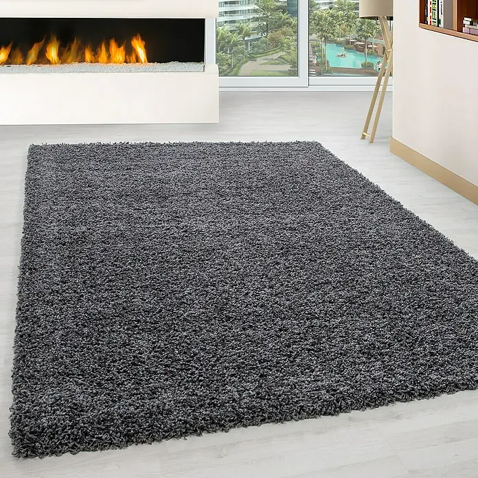 Hochflorteppich Life 1500Grau, 340 x 240 cm, 100% Polypropylen - Ein grauer, zotteliger Teppich liegt in einem modernen Wohnzimmer mit Kamin und Ausblick.