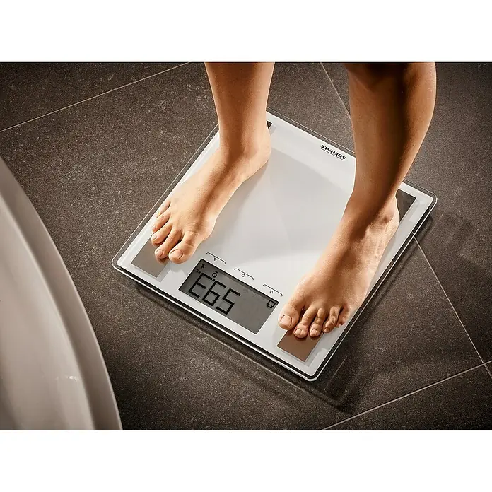 Báscula digital Shape Sense Connect 100 - 32 x 32 x 2,6 cm, Vidrio, Blanco - Una persona está de pie sobre una báscula digital Soehnle, que muestra 65,3 kg, en un suelo de baño de azulejos.