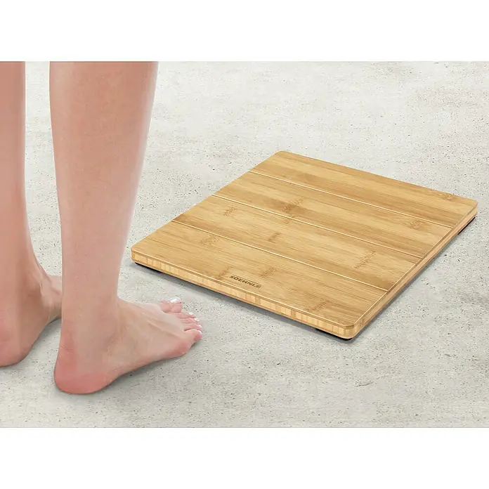 Báscula digital Style Sense Bamboo Magic - 30 x 30 x 3,3 cm, Materiales naturales, Bamboo - Una báscula personal de bambú se alza sobre un suelo gris, junto a la cual se pueden ver los pies de una persona.