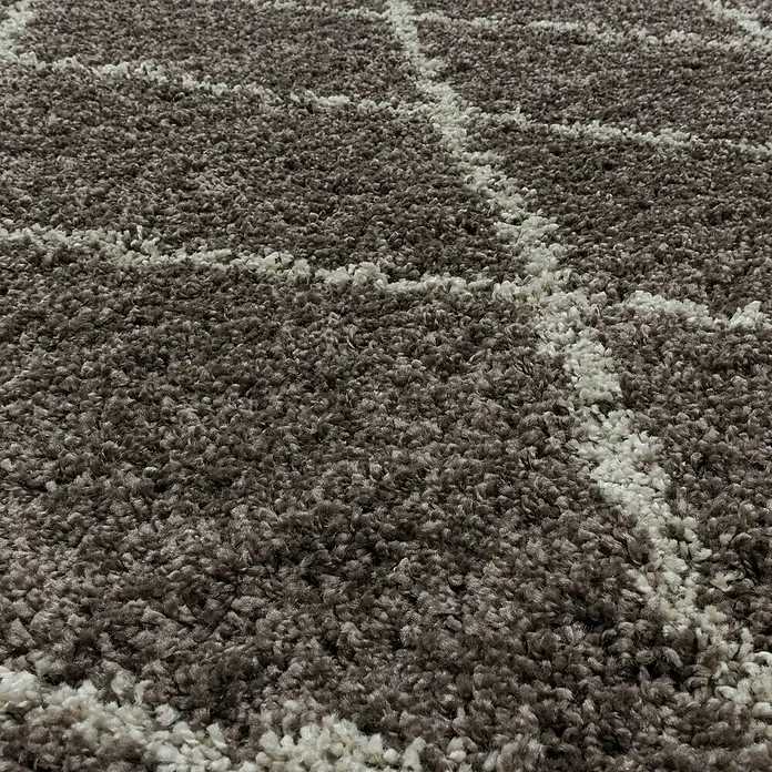 Hochflorteppich Alvor 3401Taupe, Durchmesser: 160 cm, 100 % Polypropylen - Detailaufnahme eines braunen Teppichs mit weißem geometrischem Muster, der eine weiche Textur und ein modernes Design zeigt.