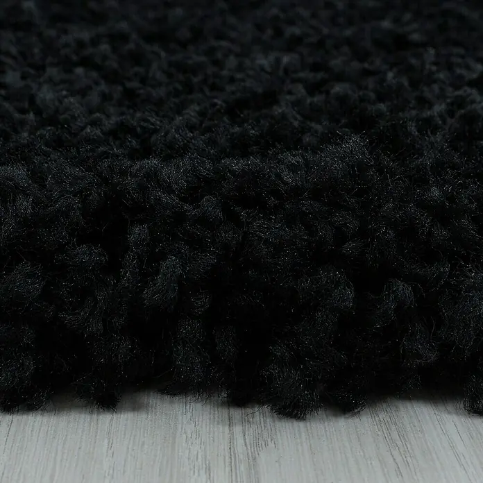Hochflorteppich Sydney 3000 - Schwarz, 110 x 60 cm, 100% Polypropylen - Nahaufnahme eines schwarzen, zotteligen Teppichs. Ideal für Wohnräume, bietet Wärme und Komfort mit seiner weichen Textur.