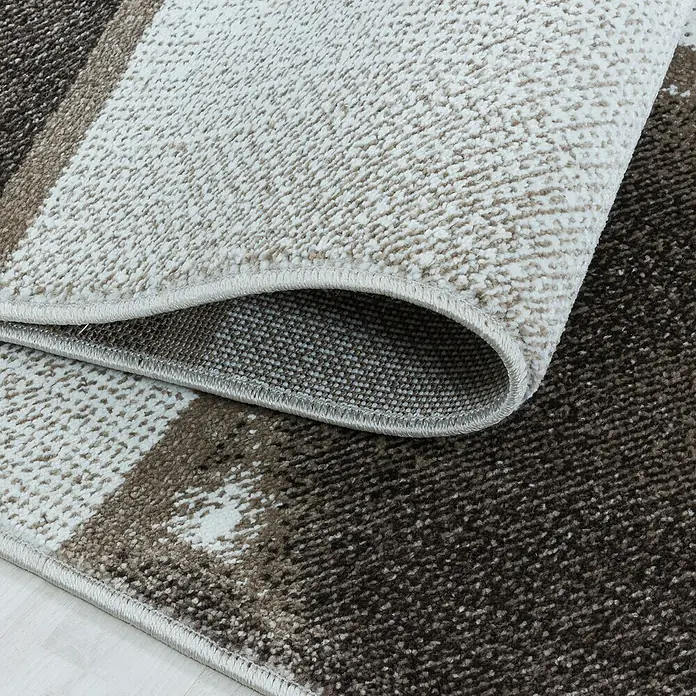Kurzflorteppich Ottawa 4201 - Braun, 200 x 140 cm, 100% Polypropylen - Nahaufnahme eines modernen Teppichs mit abstraktem Design und aufgerollter Ecke, der die Textur und Verarbeitung hervorhebt.