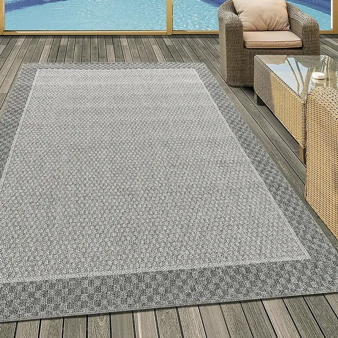 Outdoor-Teppich Aruba 4905 - Cream, 200 x 140 cm, 100% Polypropylen - Ein grauer Outdoor-Teppich mit einem geometrischen Muster liegt auf einer hölzernen Terrasse, umgeben von Gartenmöbeln.