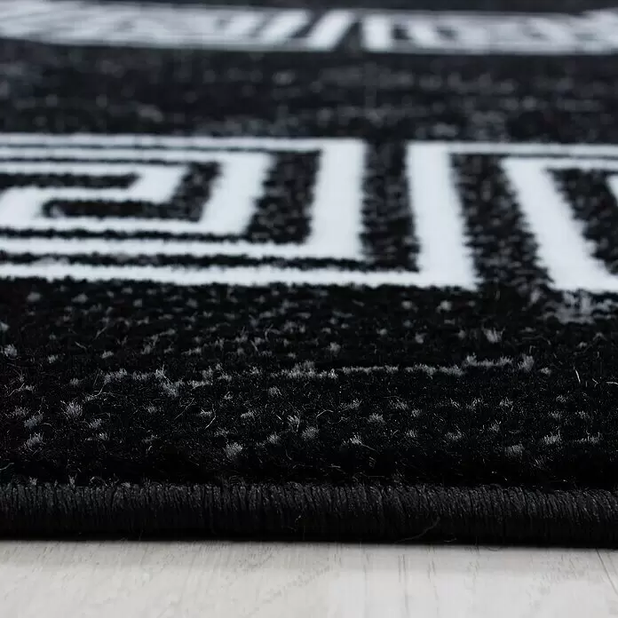 Kurzflorteppich Plus 8009 - Schwarz, 370 x 280 cm, 100 % Polypropylen - Nahaufnahme eines schwarzen Teppichs mit weißem geometrischem Muster, der seine weiche Textur und Kante zeigt.