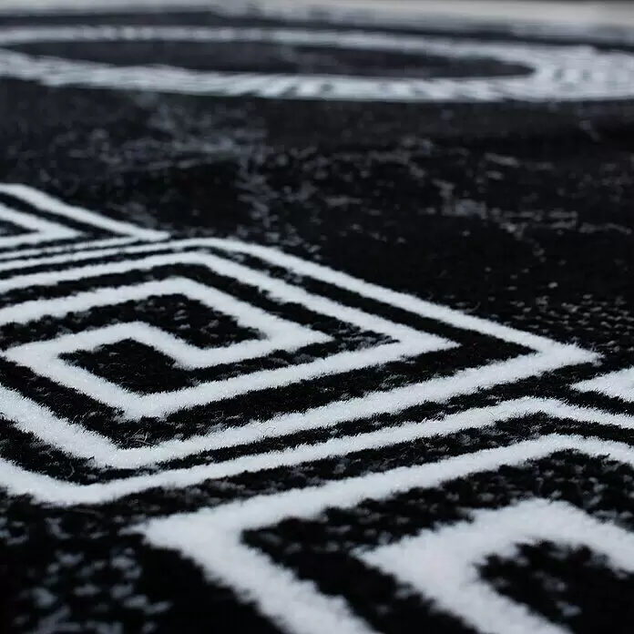 Kurzflorteppich Plus 8009 - Schwarz, 370 x 280 cm, 100 % Polypropylen - Nahaufnahme eines schwarz-weiß gemusterten Teppichs mit geometrischen Designs, die seine plüschige Textur zeigt.