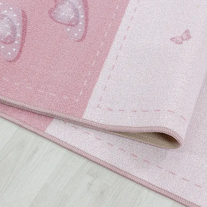 Kinderteppich Play 2905Pink, 200 x 140 cm, 100% Polyamide - Nahaufnahme eines rosa Kinderteppichs mit Herz- und Schmetterlingsmotiven, der auf einem hellen Holzboden liegt.