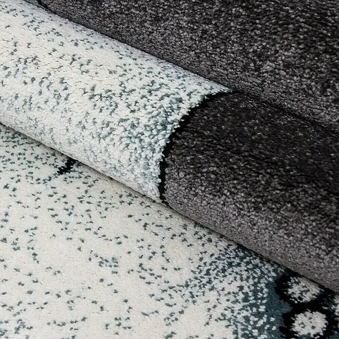 Kinderteppich Kids 0560Blau, 230 x 160 cm, 100% Polypropylen - Nahaufnahme eines gerollten Teppichs mit abstraktem Muster in Weiß-, Grau- und Schwarztönen, der eine weiche Textur und ein modernes Design zeigt.