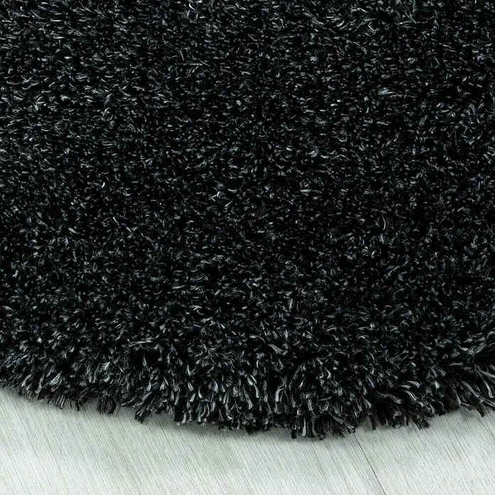 Hochflorteppich Fluffy 3500 - Anthrazit, Durchmesser: 200 cm, 100% Polypropylen - Nahaufnahme eines schwarzen, zotteligen Teppichs mit langen Fasern, der eine weiche und einladende Textur zeigt.