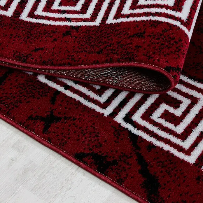 Kurzflorteppich Plus 8009 - Rot, 200 x 140 cm, 100 % Polypropylen - Nahaufnahme eines roten Teppichs mit geometrischen Mustern und einem eleganten, aufgerollten Rand.