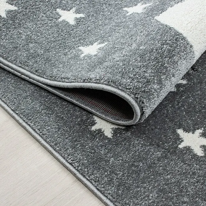 Kinderteppich Kids 0550Blau, Durchmesser: 120 cm, 100 % Polypropylen - Nahaufnahme eines grauen Teppichs mit Sternenmuster und umgeschlagener Ecke, der die Unterseite zeigt.