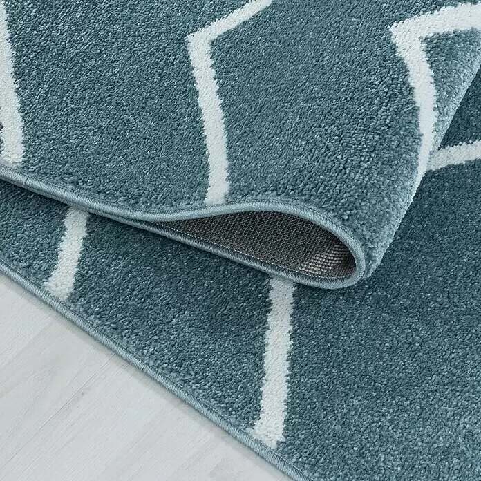 Hochflorteppich Rio 4602 - Blau, 250 x 80 cm, 100% Polypropylen - Petrolblauer Teppich mit weißem Geometriemuster, teilweise gerollt auf hellem Holzfußboden.