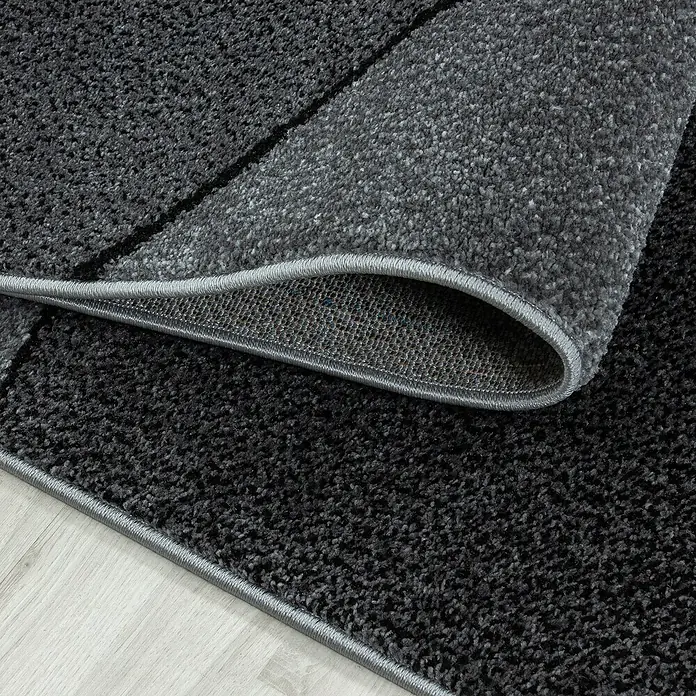 Kurzflorteppich Beta 1120Grau, 230 x 160 cm, 100 % Polypropylen - Nahaufnahme eines grauen Teppichs mit hochfloriger Textur und einer dezenten grauen Bordüre, der auf einem hellen Holzboden liegt.