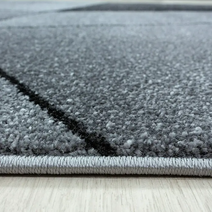 Kurzflorteppich Beta 1120Grau, 230 x 160 cm, 100 % Polypropylen - Nahaufnahme eines modernen grauen Teppichs mit abstraktem schwarzem Muster und sauberer, umrandeter Kante.