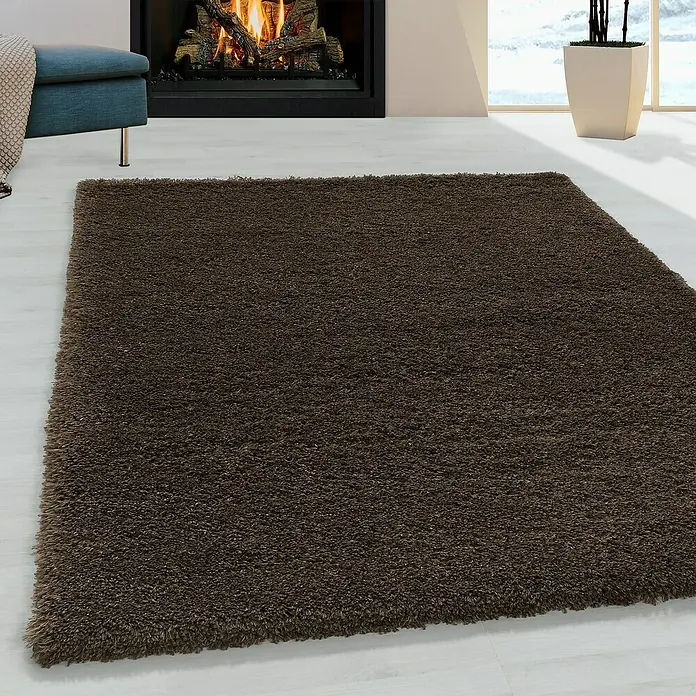 Hochflorteppich Fluffy 3500Braun, 170 x 120 cm, 100 % Polypropylen - Nahaufnahme eines zotteligen, braunen Teppichs, der Wärme und Komfort in einen Raum mit Kamin bringt.